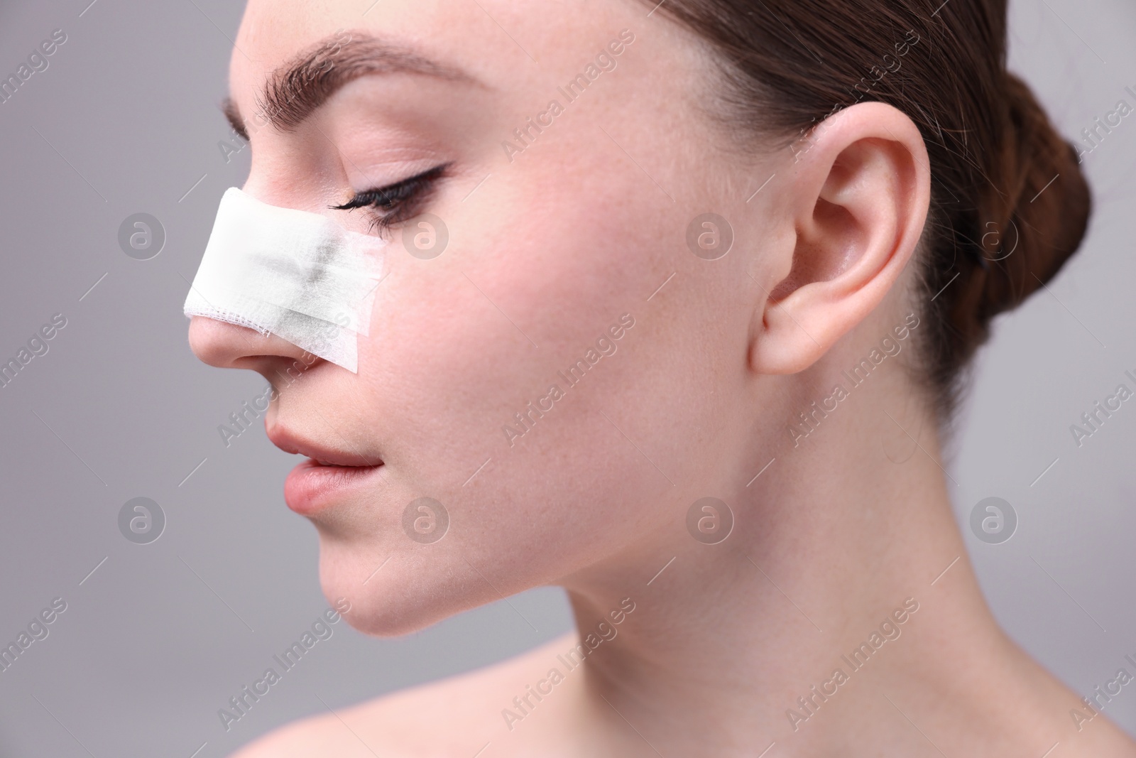 Photo of Woman with medical bandage on her nose after plastic surgery operation against grey background