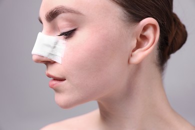 Woman with medical bandage on her nose after plastic surgery operation against grey background