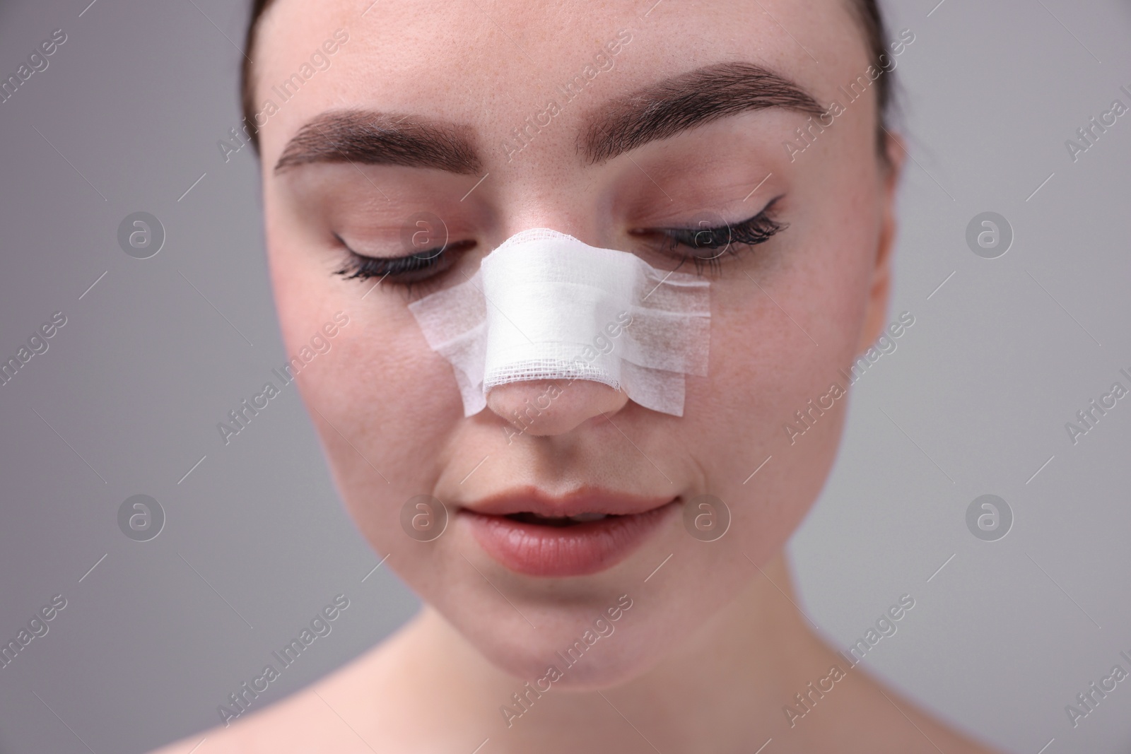 Photo of Woman with medical bandage on her nose after plastic surgery operation against grey background