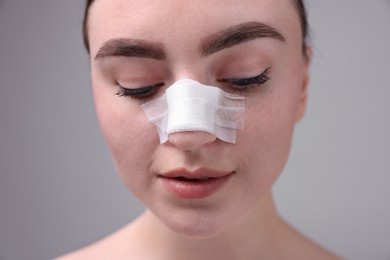 Photo of Woman with medical bandage on her nose after plastic surgery operation against grey background