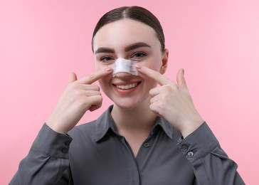 Woman with medical bandage on her nose after plastic surgery operation against pink background