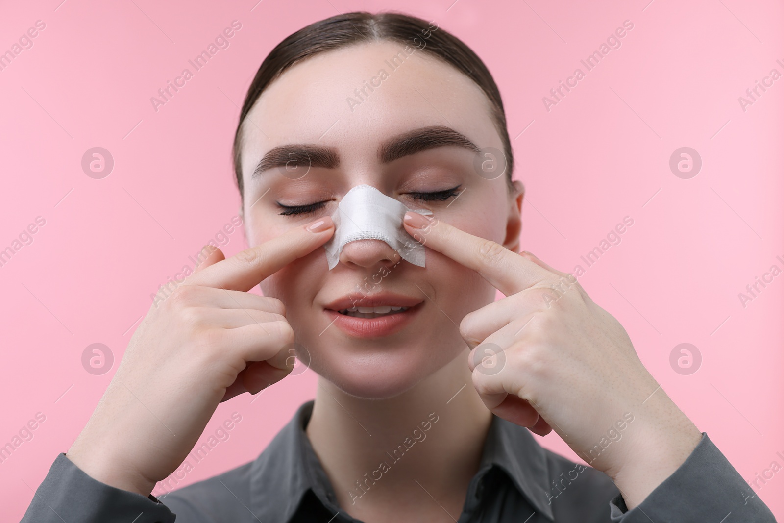 Photo of Woman with medical bandage on her nose after plastic surgery operation against pink background