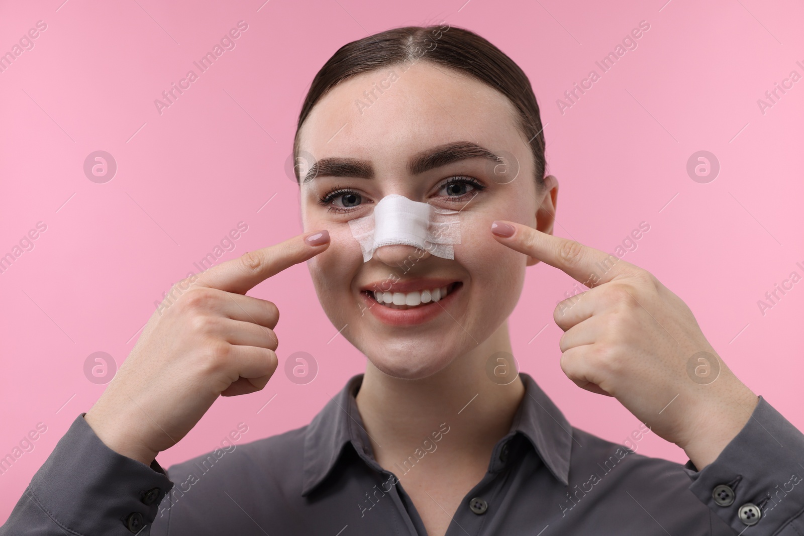 Photo of Woman with medical bandage on her nose after plastic surgery operation against pink background