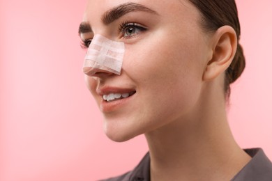 Woman with medical bandage on her nose after plastic surgery operation against pink background, , closeup