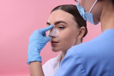 Photo of Doctor checking patient's nose after plastic surgery operation on pink background, closeup