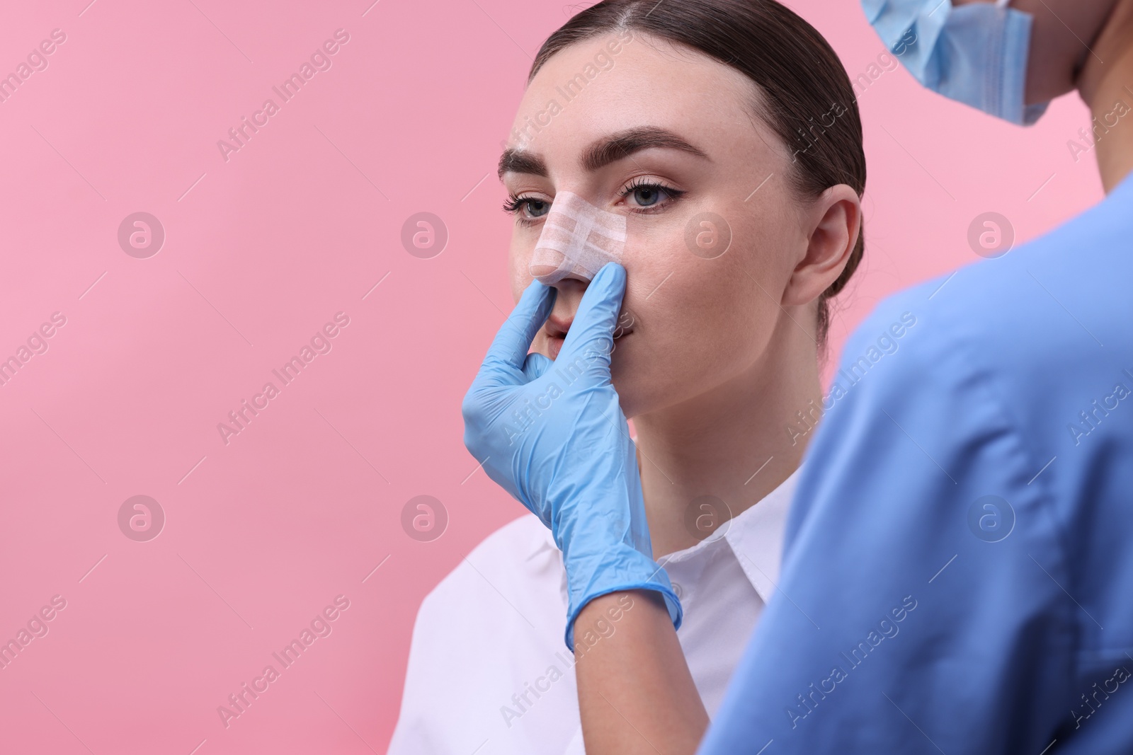 Photo of Doctor checking patient's nose after plastic surgery operation on pink background, closeup. Space for text