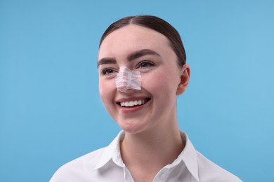 Photo of Woman with medical bandage on her nose after plastic surgery operation against light blue background