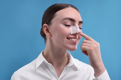 Photo of Woman with medical bandage on her nose after plastic surgery operation against light blue background