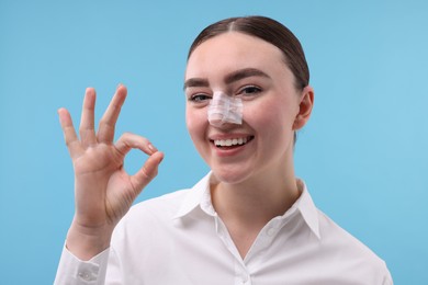 Photo of Woman with medical bandage on her nose after plastic surgery operation against light blue background