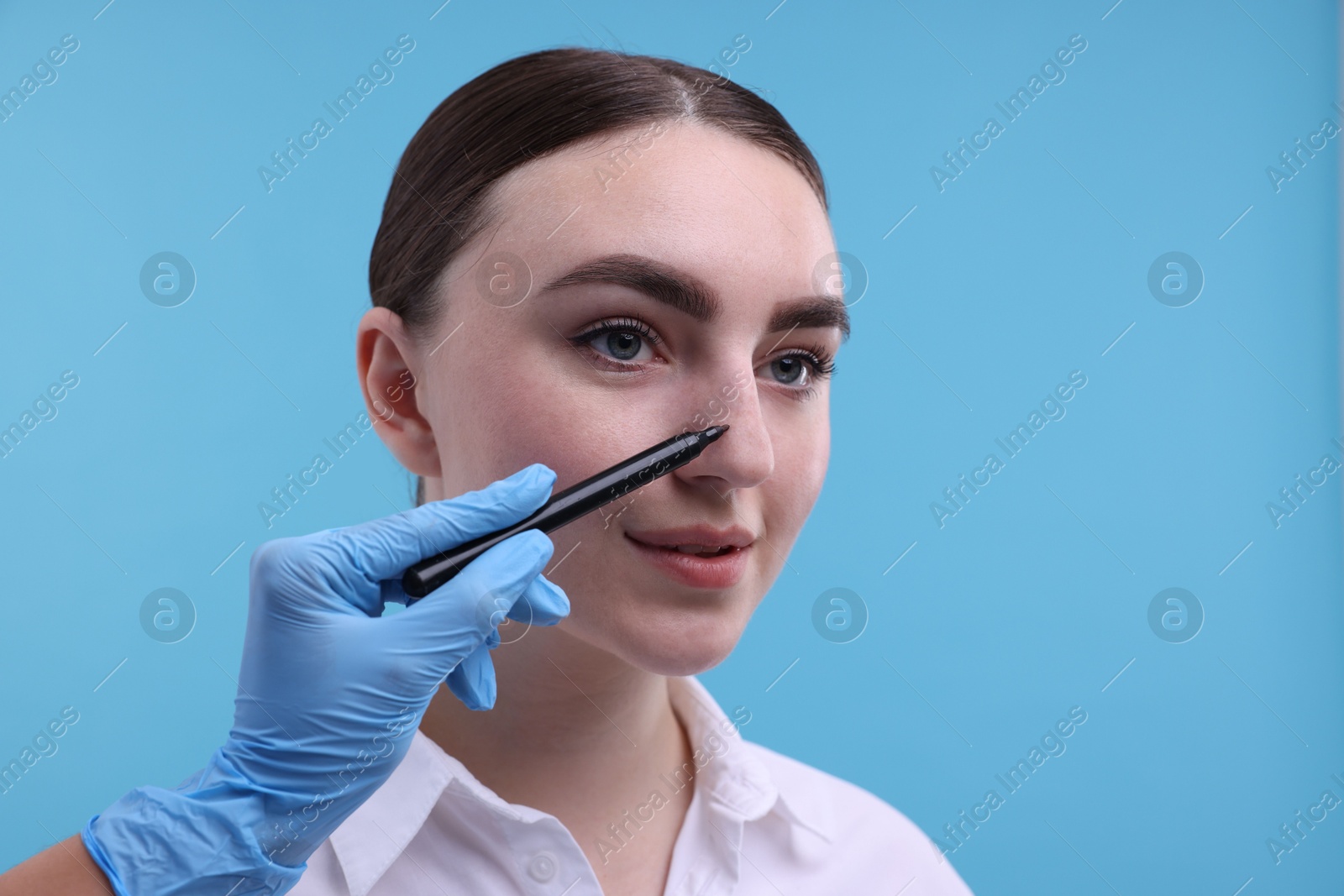 Photo of Doctor drawing marks on patient's nose for plastic surgery operation against light blue background, , closeup. Space for text