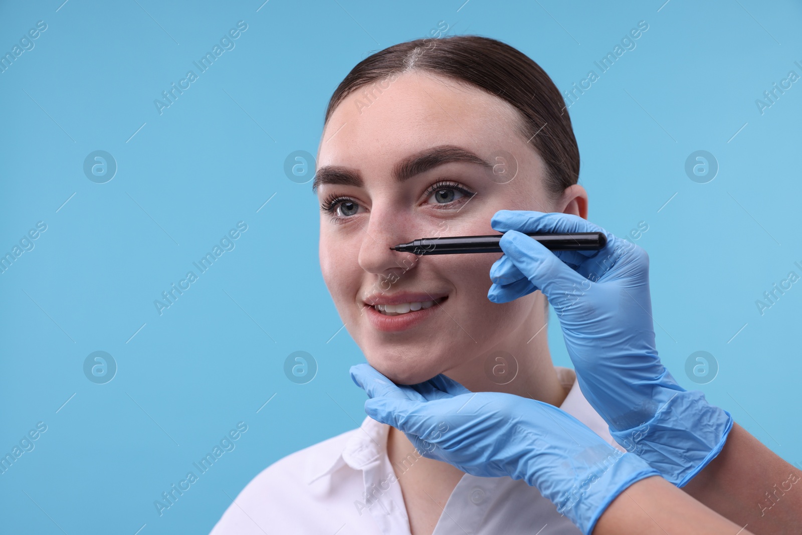 Photo of Doctor drawing marks on patient's nose for plastic surgery operation against light blue background, , closeup. Space for text