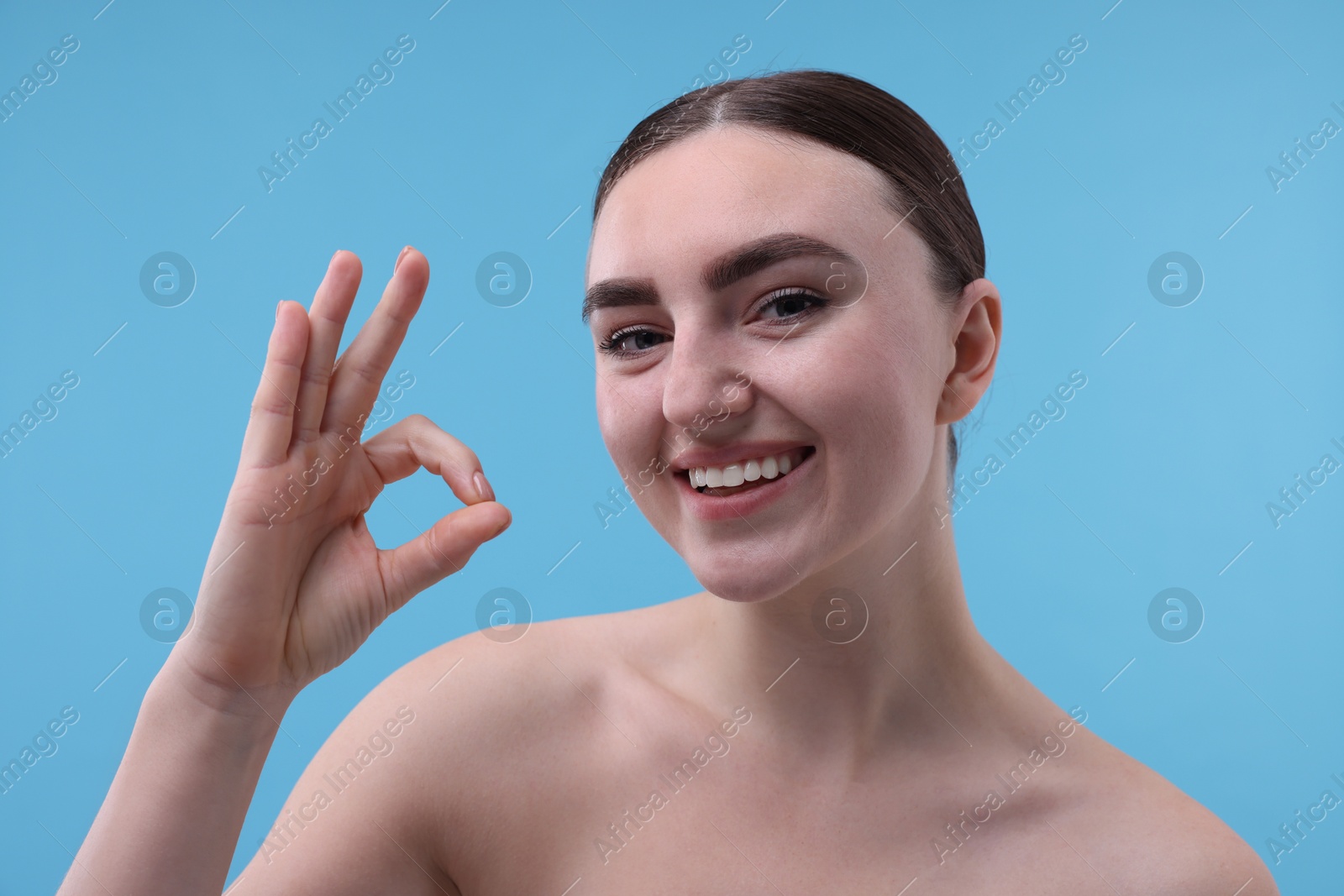 Photo of Beautiful woman showing ok gesture on light blue background