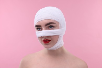 Photo of Woman with nose wrapped in medical bandage after plastic surgery operation on pink background