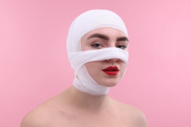 Photo of Woman with nose wrapped in medical bandage after plastic surgery operation on pink background