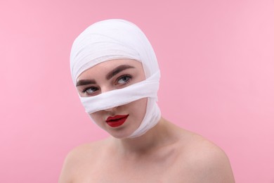 Photo of Woman with nose wrapped in medical bandage after plastic surgery operation on pink background