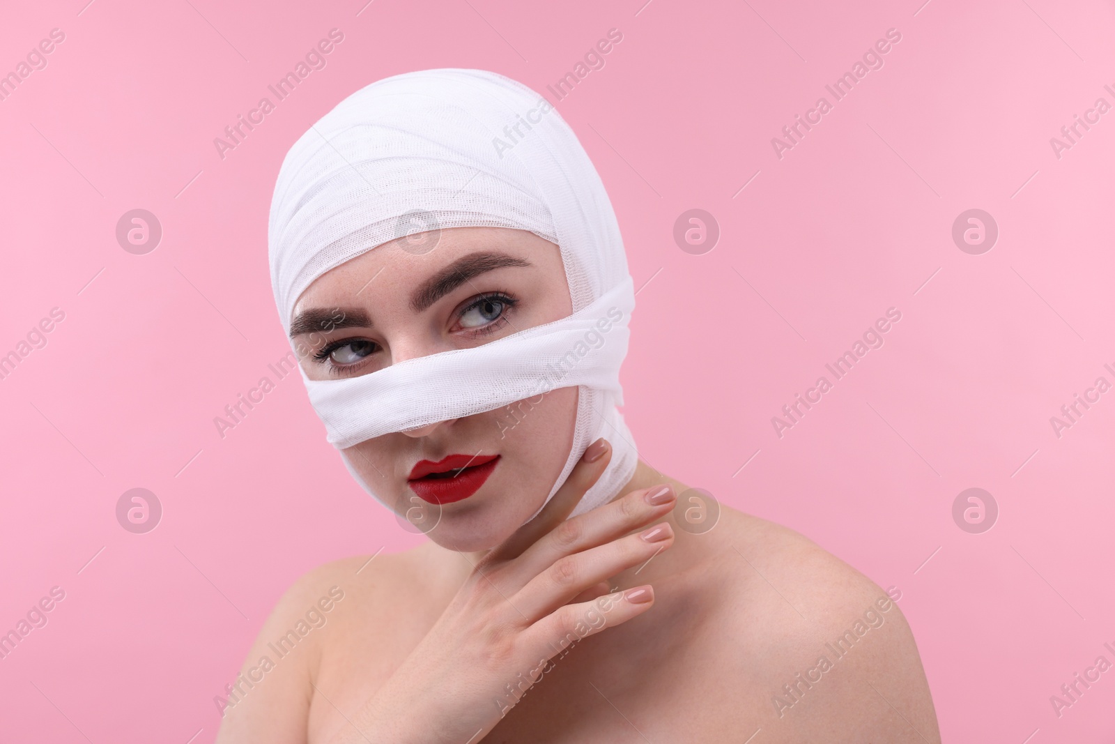 Photo of Woman with nose wrapped in medical bandage after plastic surgery operation on pink background