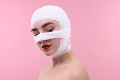 Photo of Woman with nose wrapped in medical bandage after plastic surgery operation on pink background