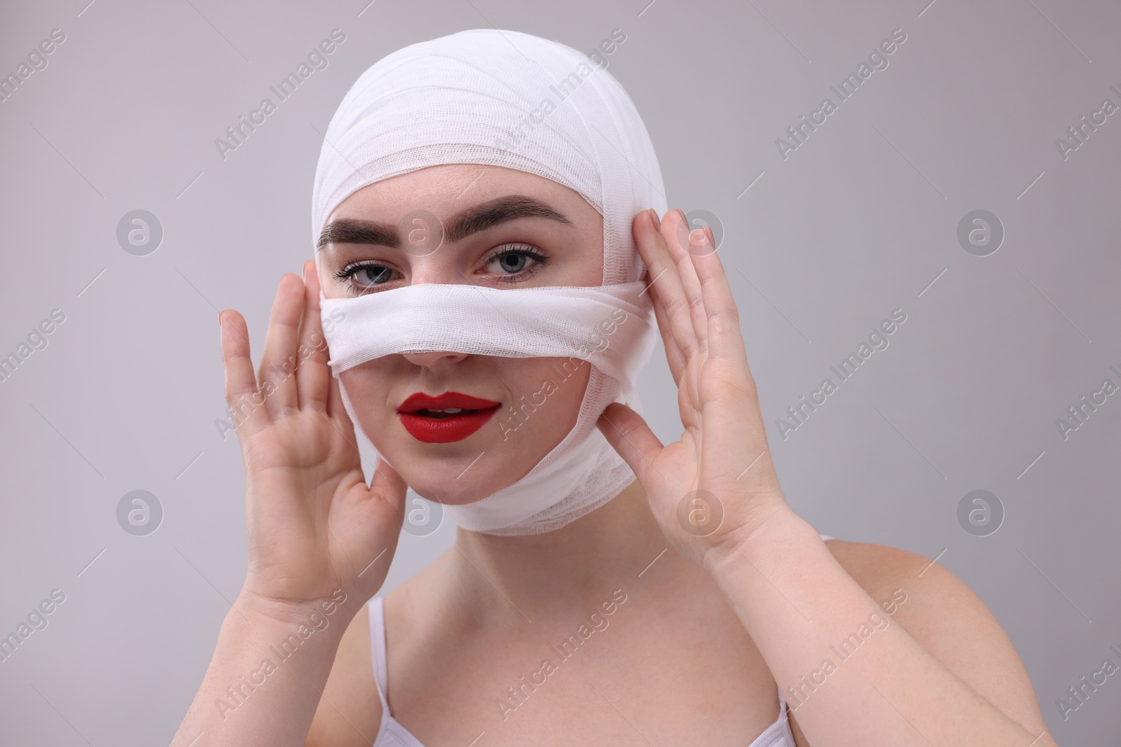 Photo of Woman with nose wrapped in medical bandage after plastic surgery operation on grey background