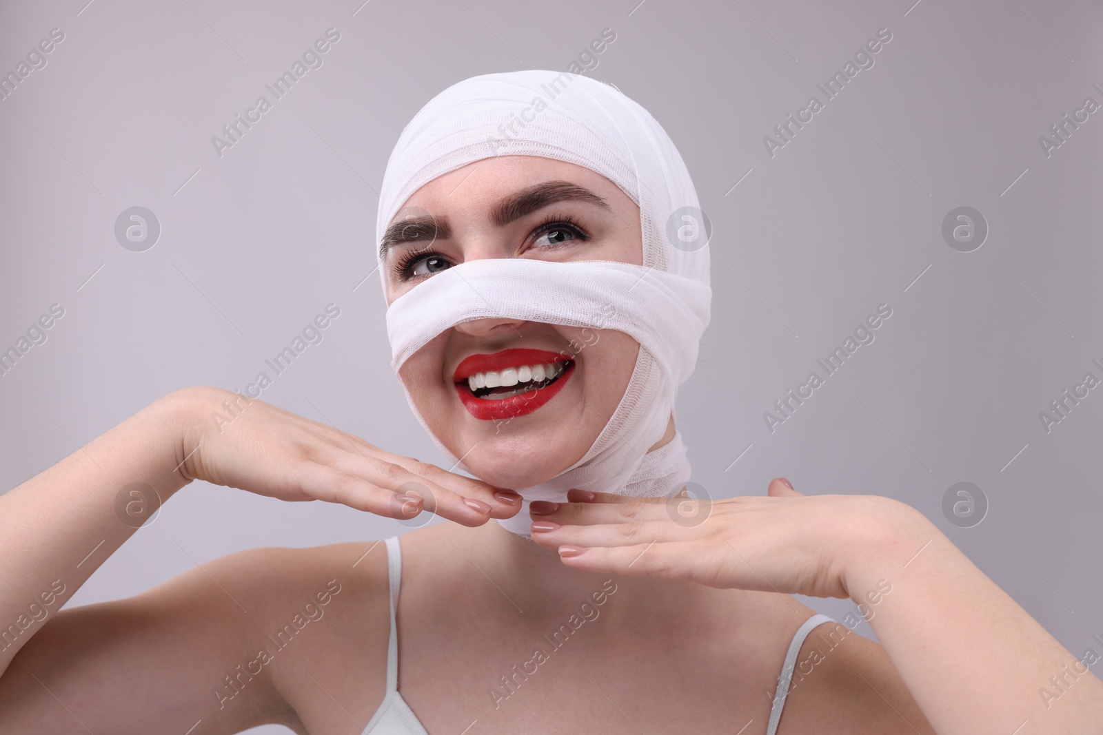 Photo of Woman with nose wrapped in medical bandage after plastic surgery operation on grey background