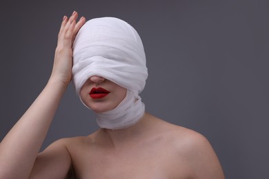 Woman with face wrapped in medical bandage after plastic surgery operation on grey background