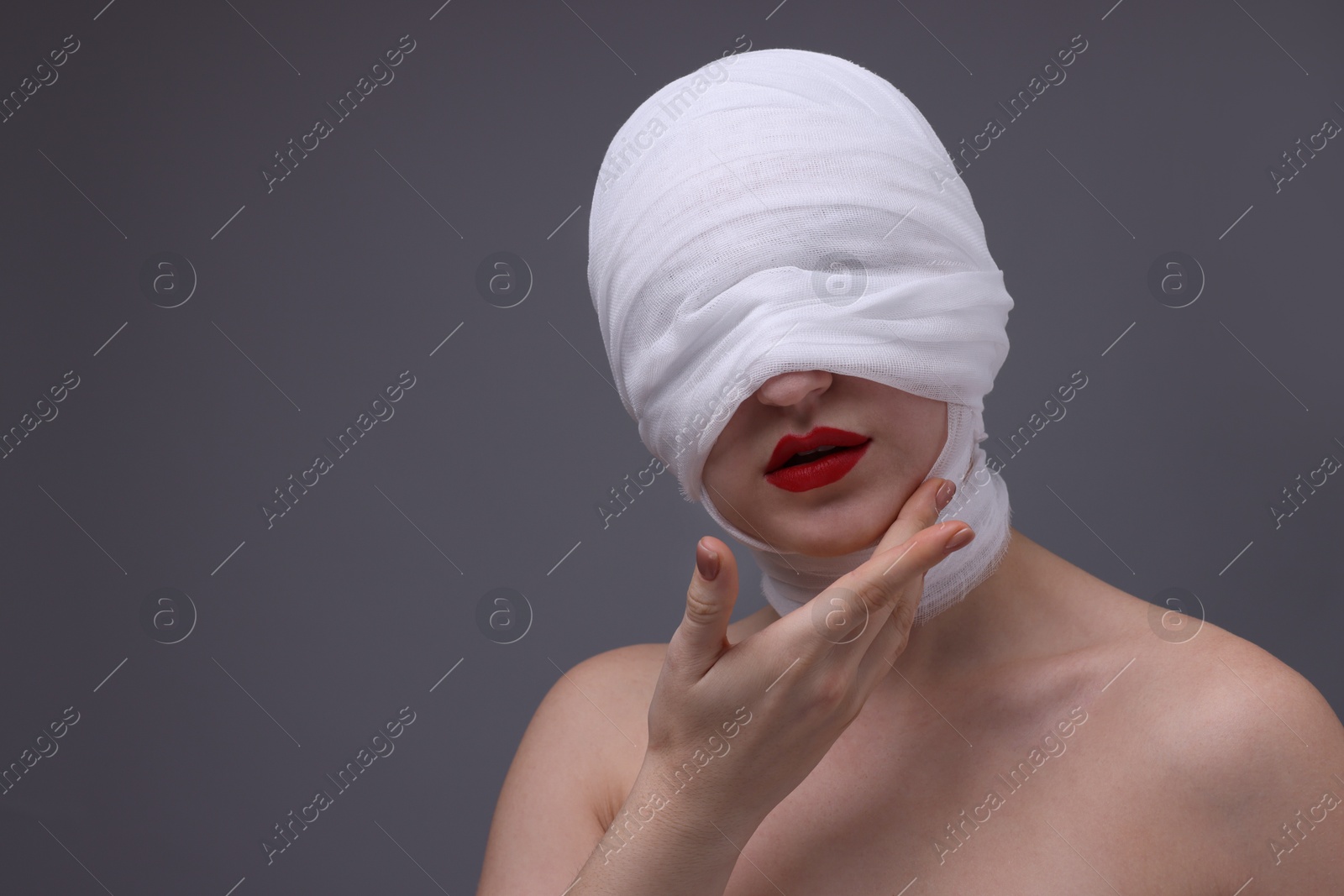 Photo of Woman with face wrapped in medical bandage after plastic surgery operation on grey background, space for text