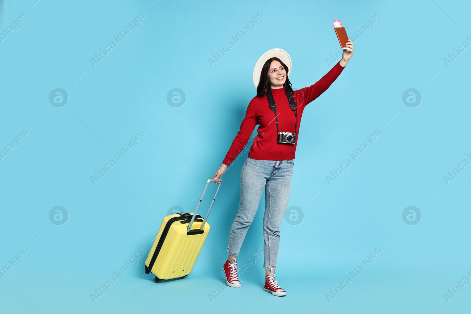 Photo of Young tourist in hat with camera, passport, tickets and suitcase on light blue background