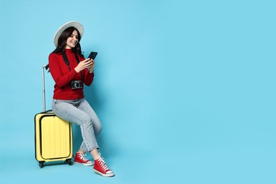 Photo of Young tourist in hat with camera, phone and suitcase on light blue background, space for text