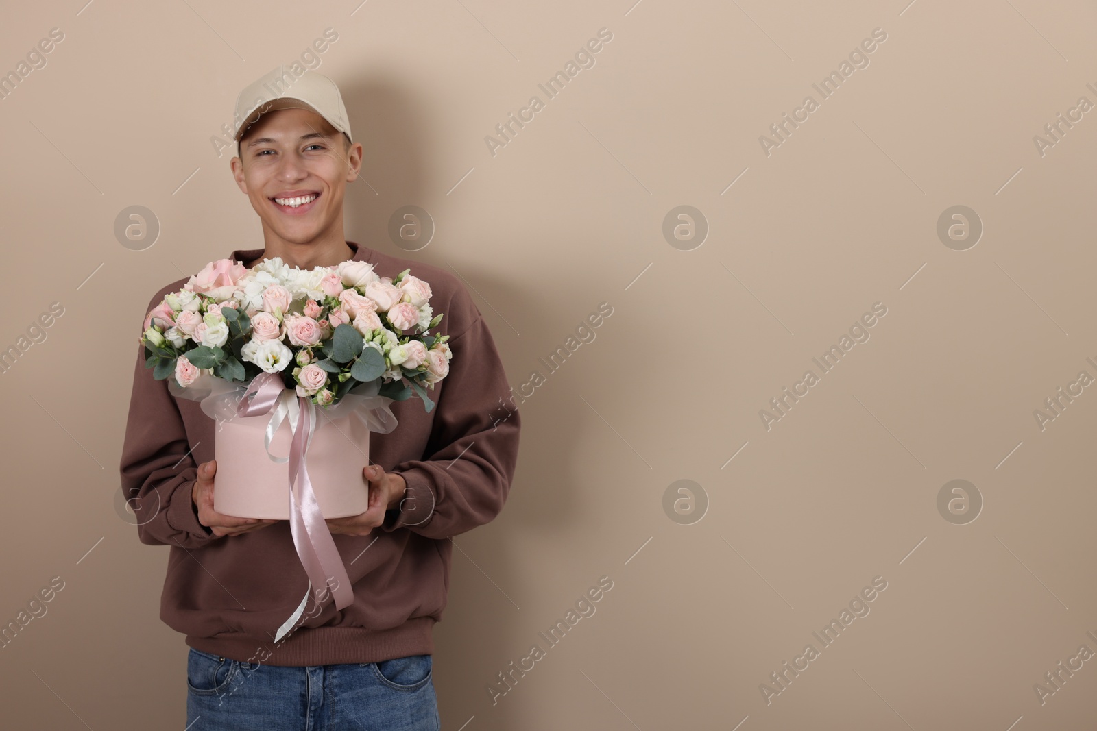 Photo of Smiling delivery man holding gift box with beautiful floral composition on beige background. Space for text