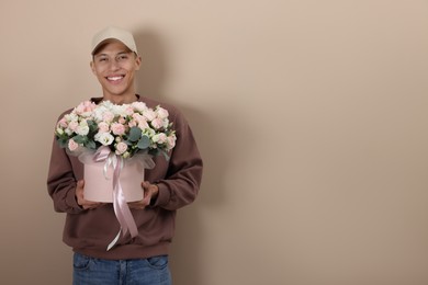 Smiling delivery man holding gift box with beautiful floral composition on beige background. Space for text