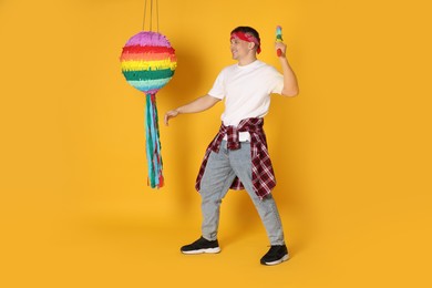 Photo of Happy man breaking pinata on yellow background