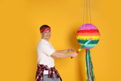 Photo of Happy man breaking pinata on yellow background