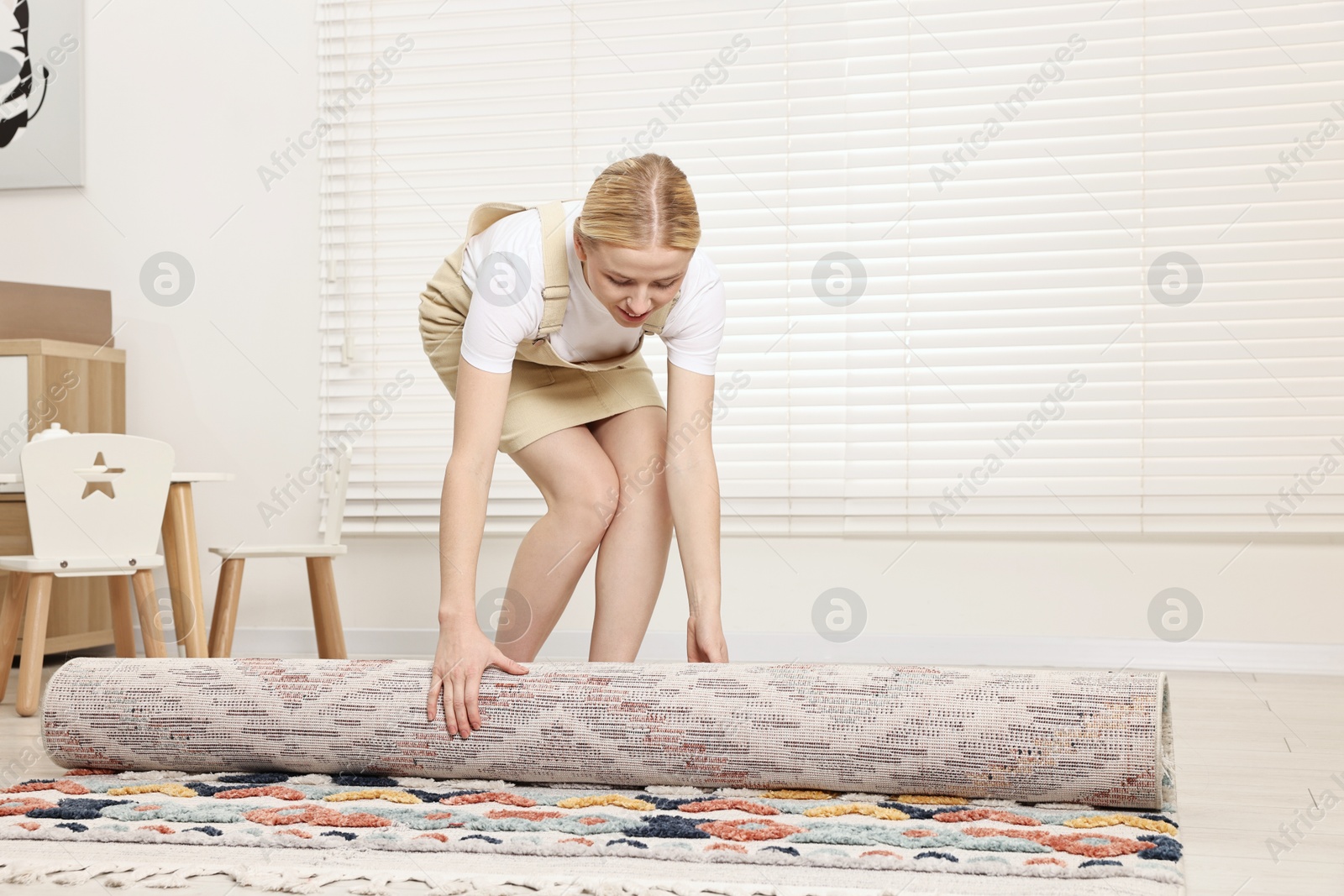 Photo of Happy decorator rolling out carpet in child's room. Space for text