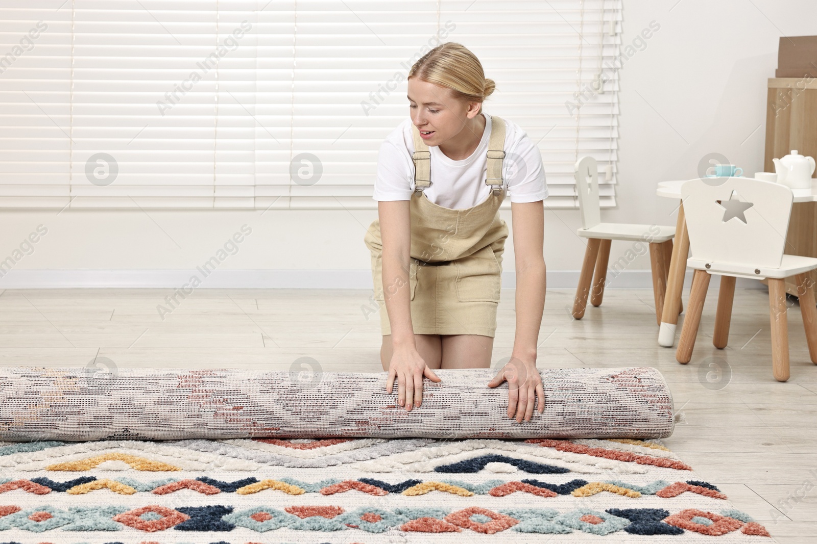 Photo of Happy decorator rolling out carpet in child's room. Space for text