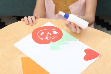 Photo of Girl applying glue onto paper figure for her creative project at table indoors, closeup. Art and craft