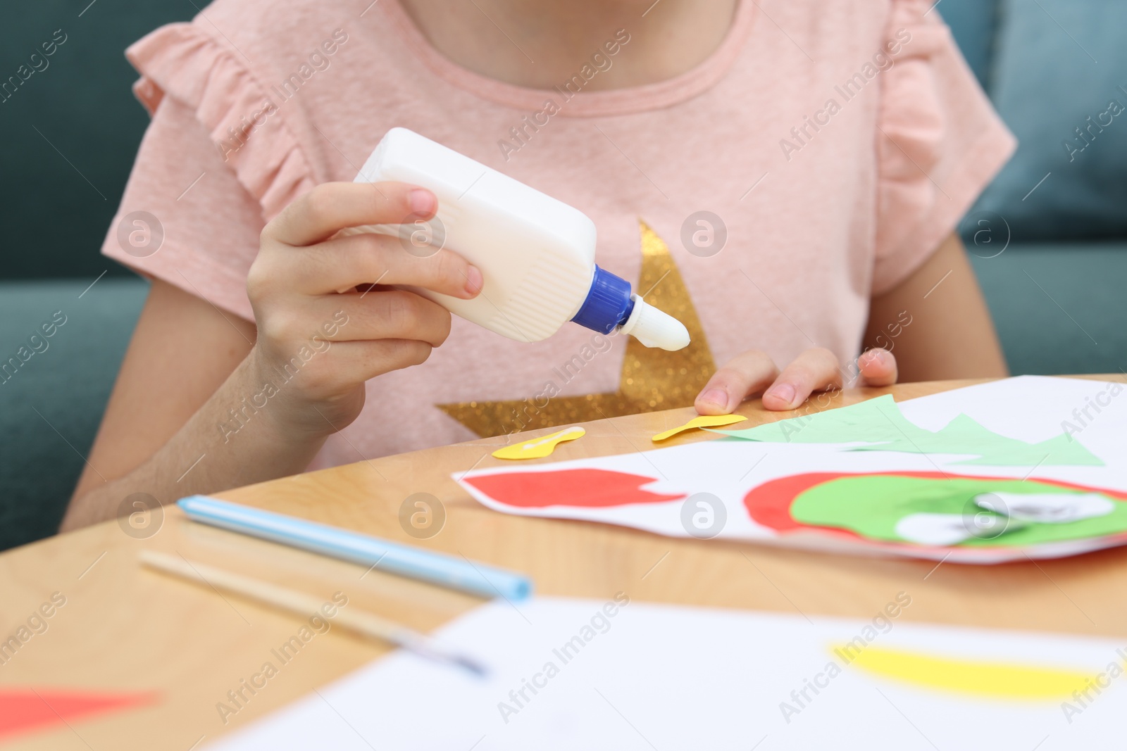 Photo of Girl applying glue onto paper figure for her creative project at table indoors, closeup. Art and craft