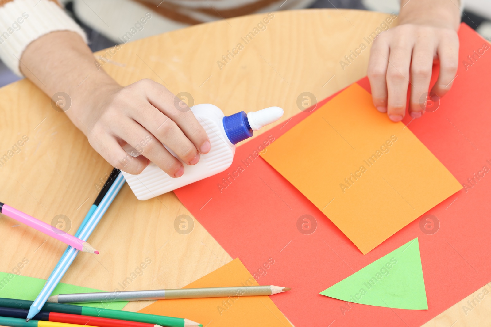 Photo of Girl applying glue onto paper figure for her creative project at table indoors, closeup. Art and craft