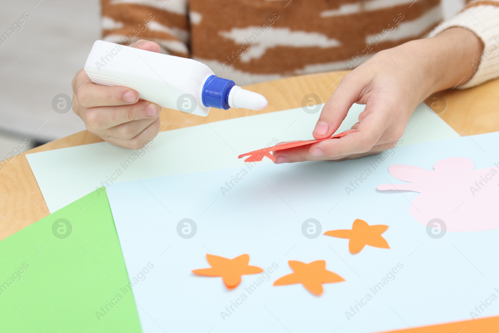 Photo of Girl applying glue onto paper figure for her creative project at table indoors, closeup. Art and craft