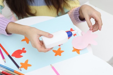 Photo of Girl applying glue onto paper figure for her creative project at table indoors, closeup. Art and craft