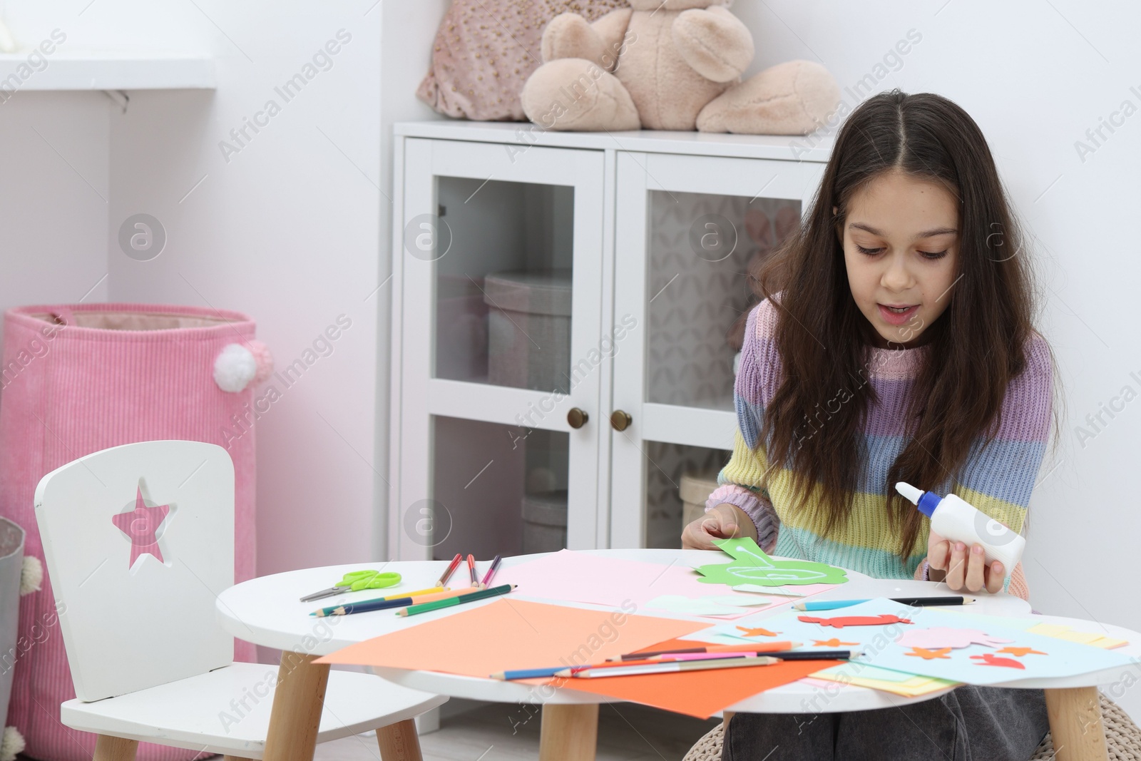 Photo of Girl applying glue onto paper figure for her creative project at table indoors. Art and craft