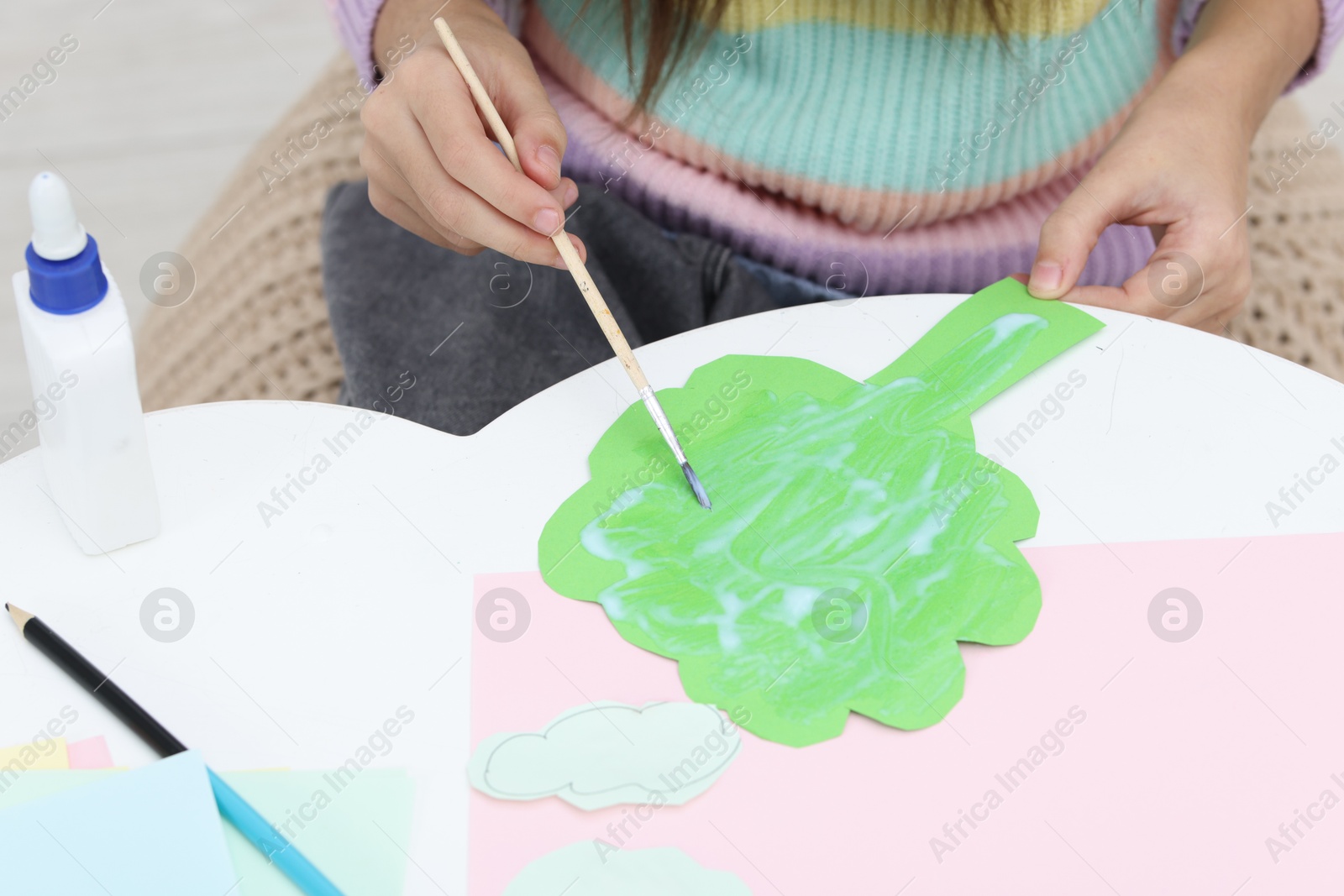 Photo of Girl applying glue onto paper figure for her creative project at table indoors, closeup. Art and craft