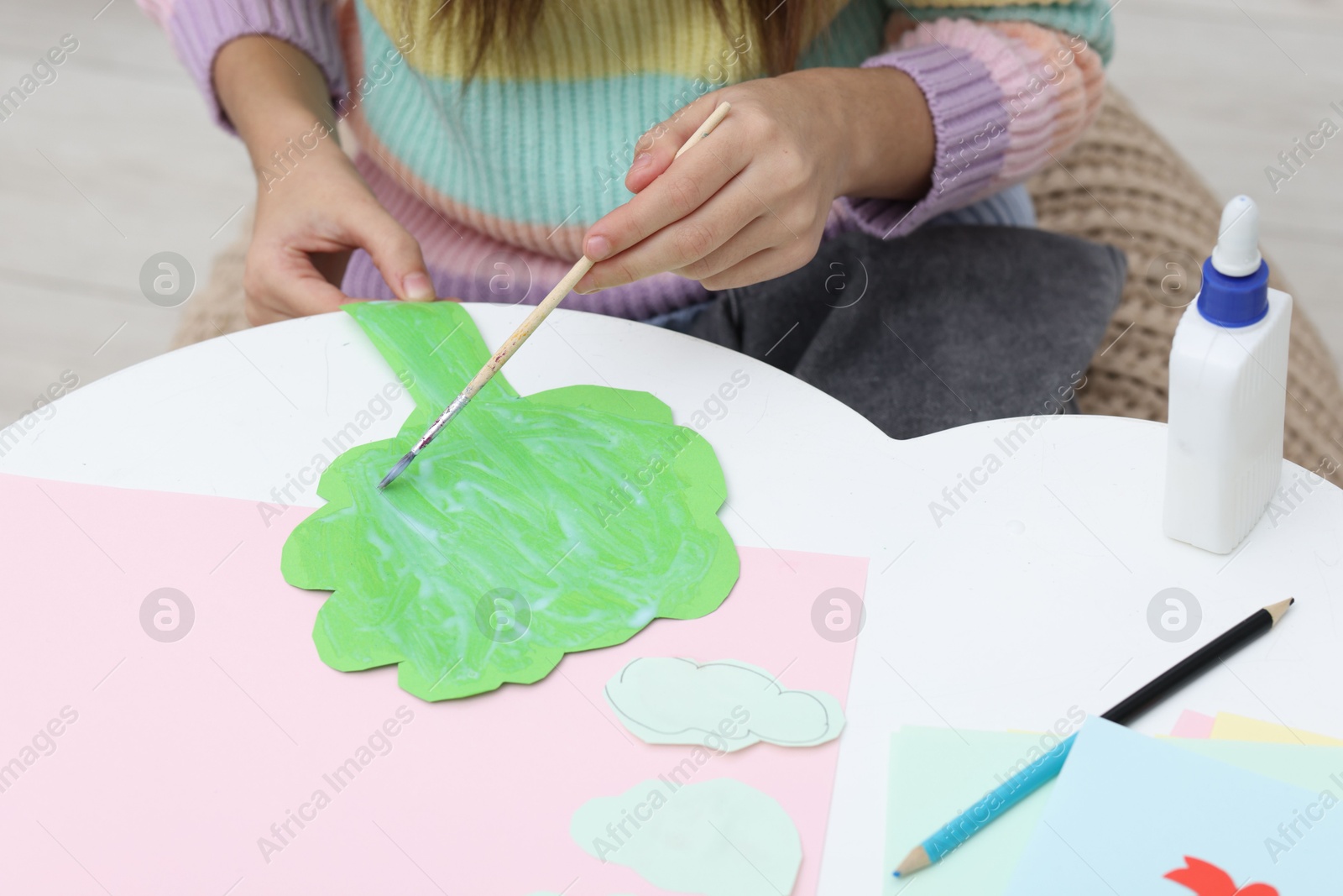 Photo of Girl applying glue onto paper figure for her creative project at table indoors, closeup. Art and craft