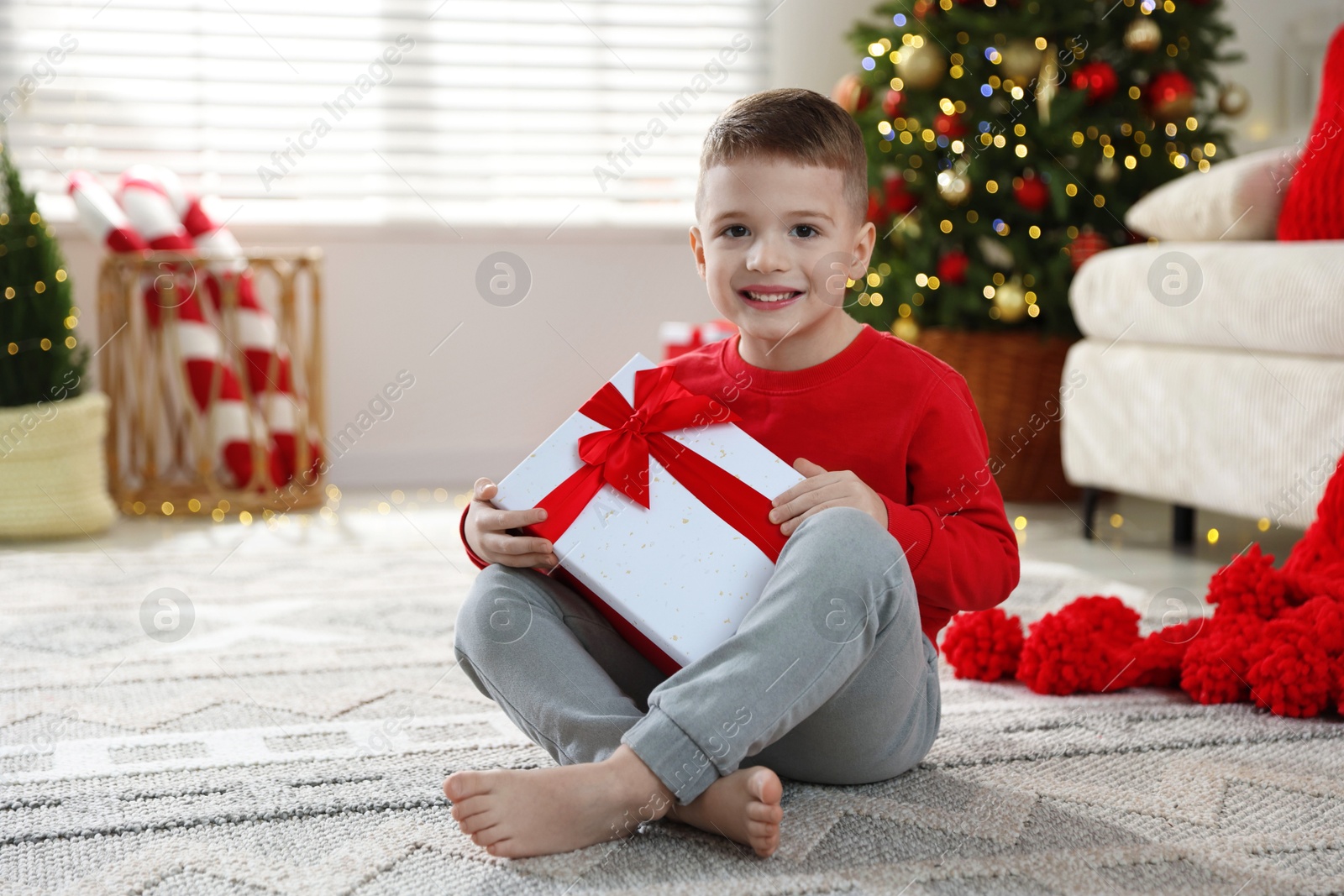 Photo of Happy little boy with Christmas gift on floor at home