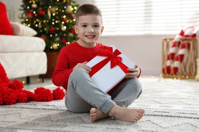 Photo of Happy little boy with Christmas gift on floor at home