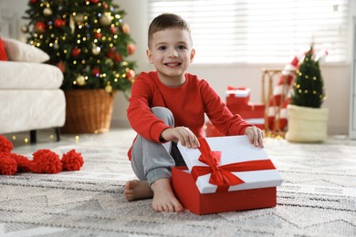 Photo of Happy little boy with Christmas gift on floor at home