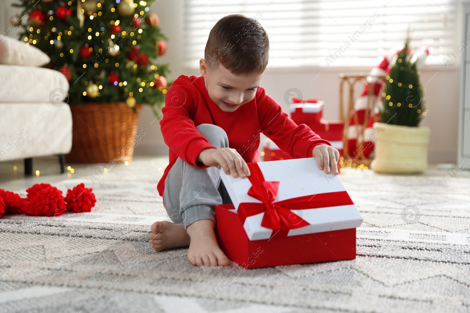 Photo of Happy little boy with Christmas gift on floor at home