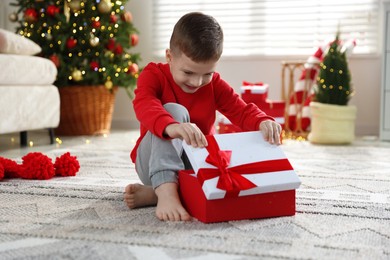 Photo of Happy little boy with Christmas gift on floor at home