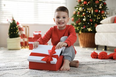 Photo of Happy little boy with Christmas gift on floor at home