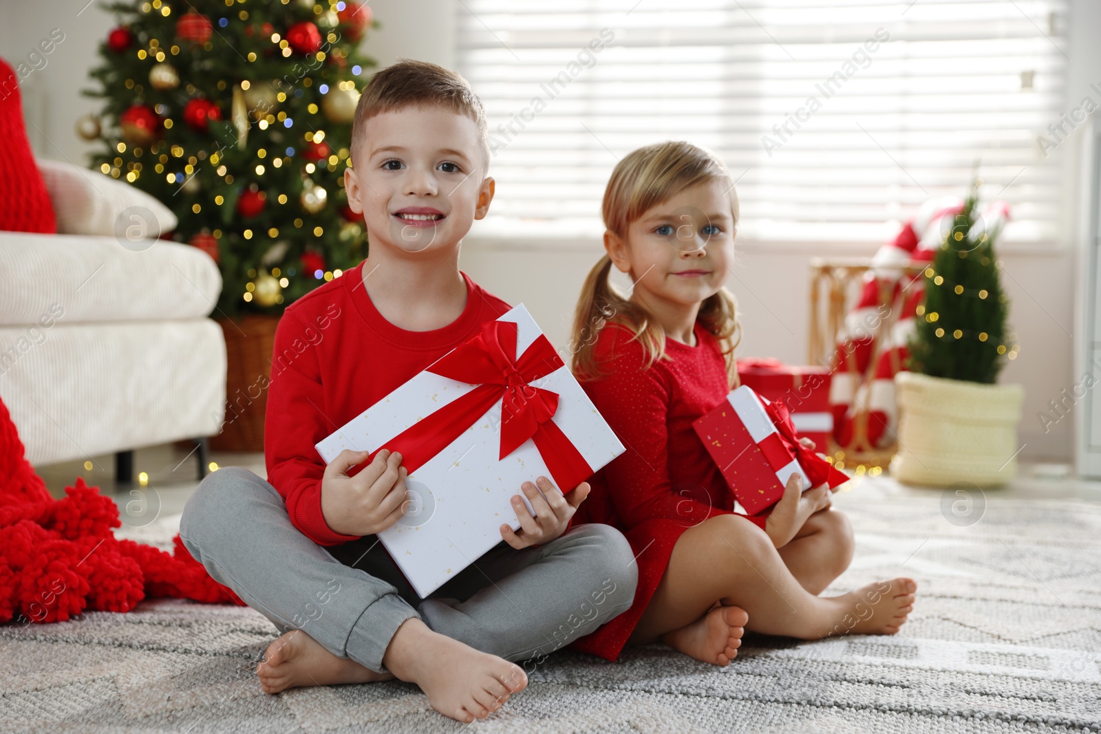 Photo of Happy little children with Christmas gifts on floor at home