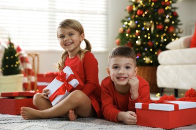 Photo of Happy little children with Christmas gifts on floor at home