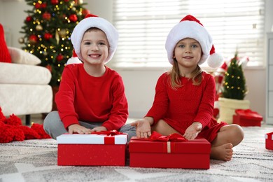 Happy little children in Santa hats with Christmas gifts on floor at home